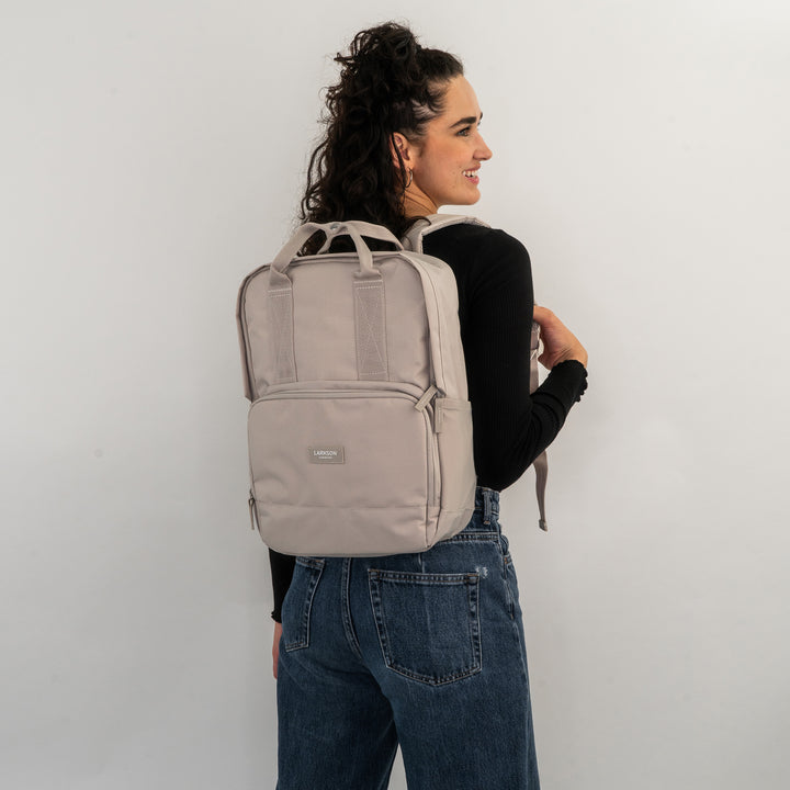 Beiger LARKSON Rucksack No 6 aus rechteckigem Stoff mit Vorderfach, getragen von Frau in schwarzem Oberteil und blauen Jeans