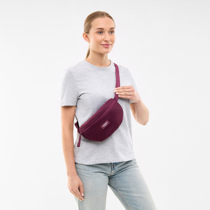 Frau trägt LARKSON Bauchtasche Finn in Beerenton über der Schulter zu grauem T-Shirt und Jeans