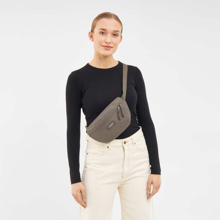 Frau trägt Bauchtasche Finn in gravel über der Schulter, schwarzes Langarmshirt, helle Jeans