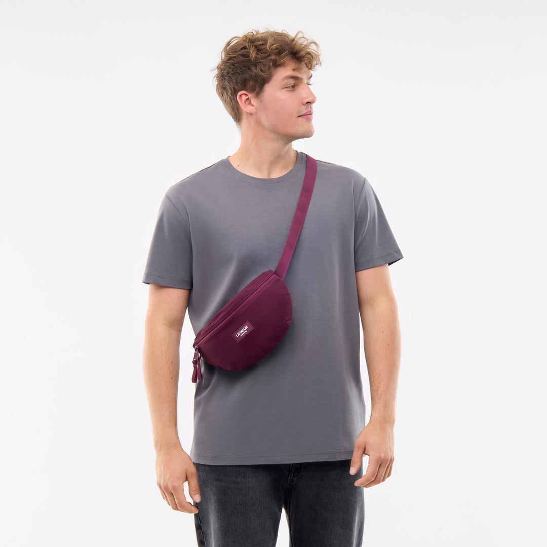 Mann mit grauem T-Shirt trägt eine bordeauxfarbene Bauchtasche Finn von LARKSON quer über die Schulter