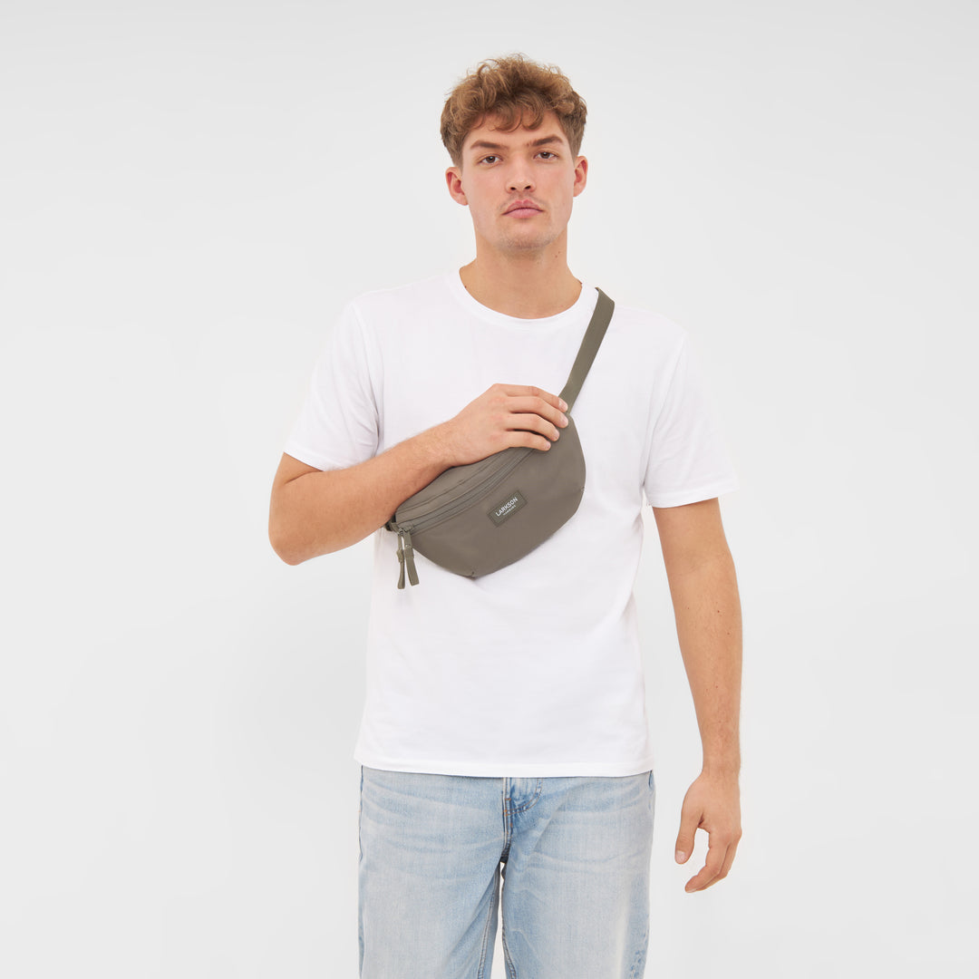 Mann trägt graue LARKSON Bauchtasche Finn über der Schulter, weiße T-Shirt, helle Jeans