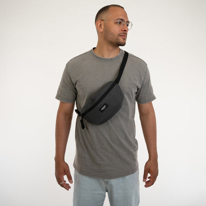 Mann trägt anthrazitgraue LARKSON Bauchtasche Finn über der Schulter mit grauem T-Shirt und hellblauen Jeans