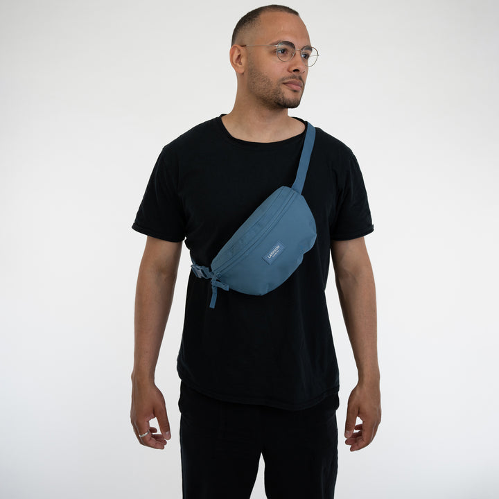 Mann trägt blaue LARKSON Bauchtasche Finn diagonlal vor der Brust, schwarzes T-Shirt
