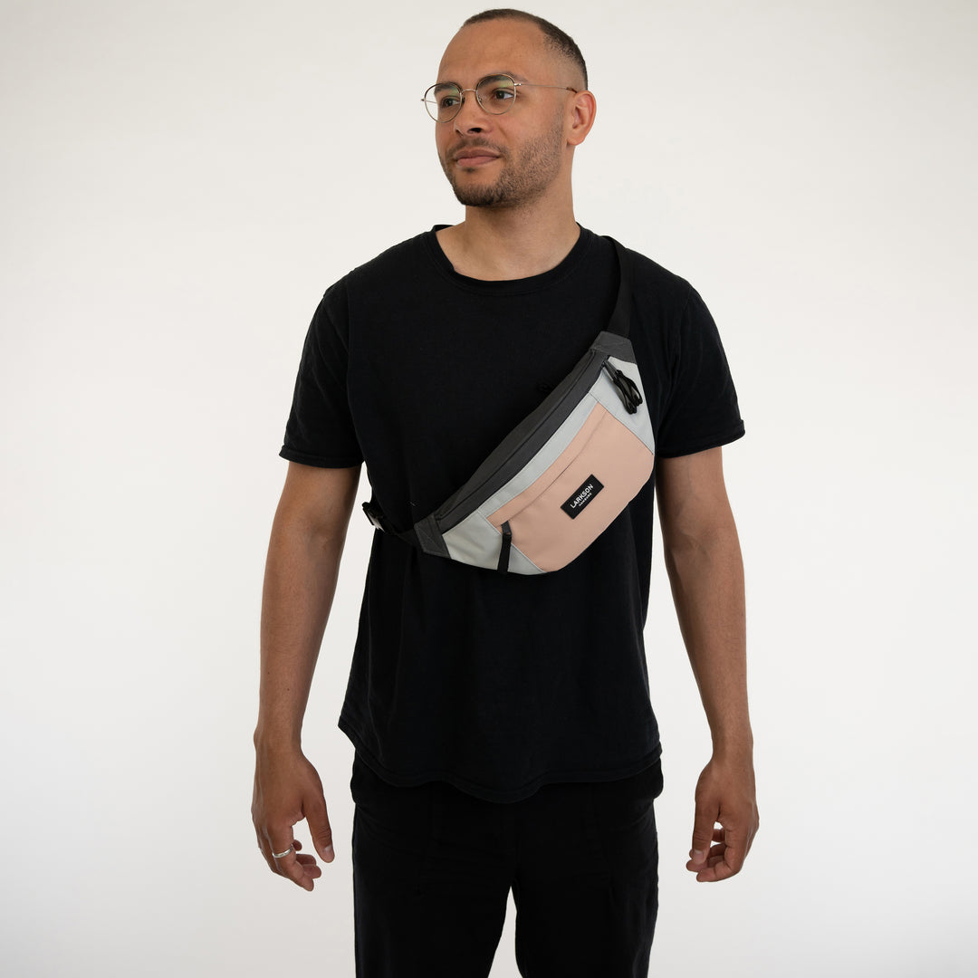 Mann trägt Bauchtasche Ole von Larkson in Grau und Rosa über der Schulter, schwarzes T-Shirt