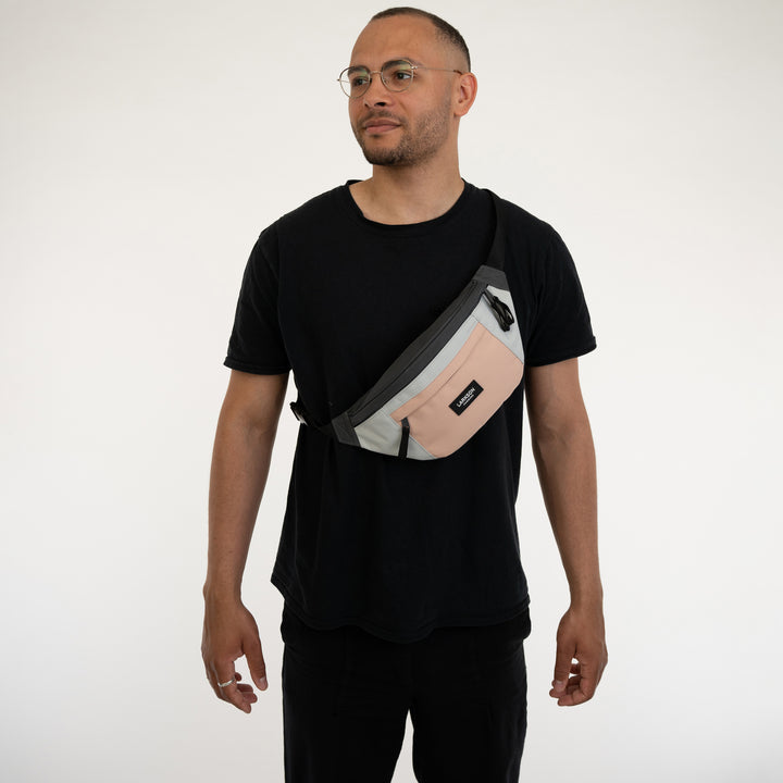Mann trägt Bauchtasche Ole von Larkson in Grau und Rosa über der Schulter, schwarzes T-Shirt