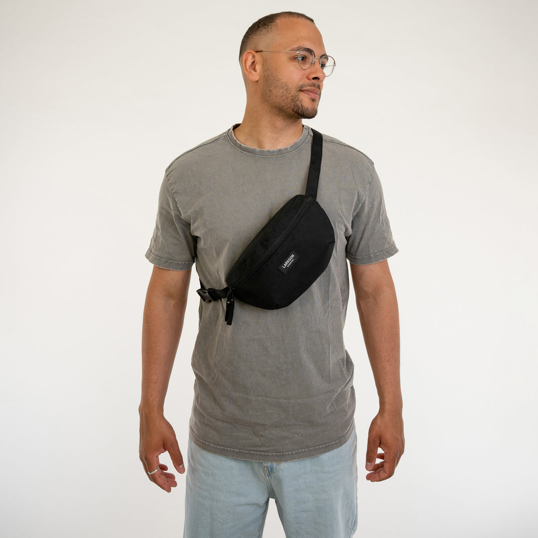 Mann trägt schwarze Larkson Bauchtasche Finn quer über Brust, graues T-Shirt, helle Jeans