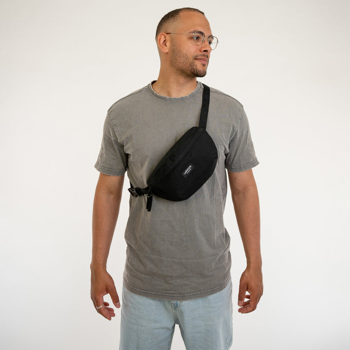 Mann trägt schwarze Larkson Bauchtasche Finn quer über Brust, graues T-Shirt, helle Jeans