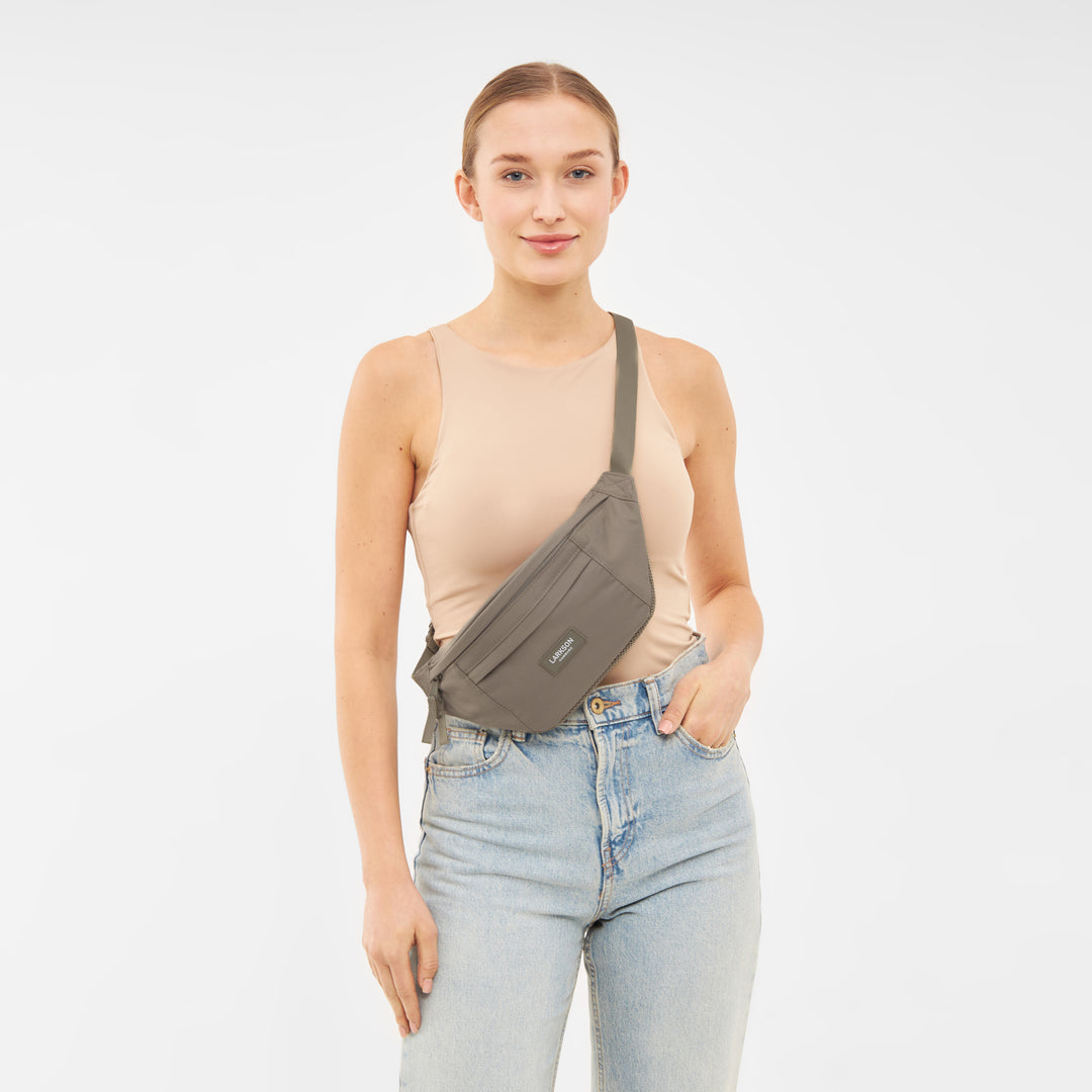 Frau trägt beige Bauchtasche Ole von Larkson quer über dem Oberkörper mit beigem Top und blauen Jeans