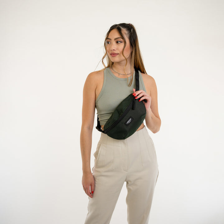 Frau trägt grüne Bauchtasche Finn von LARKSON über die Schulter, kombiniert mit grünem Tanktop und hellen Hosen