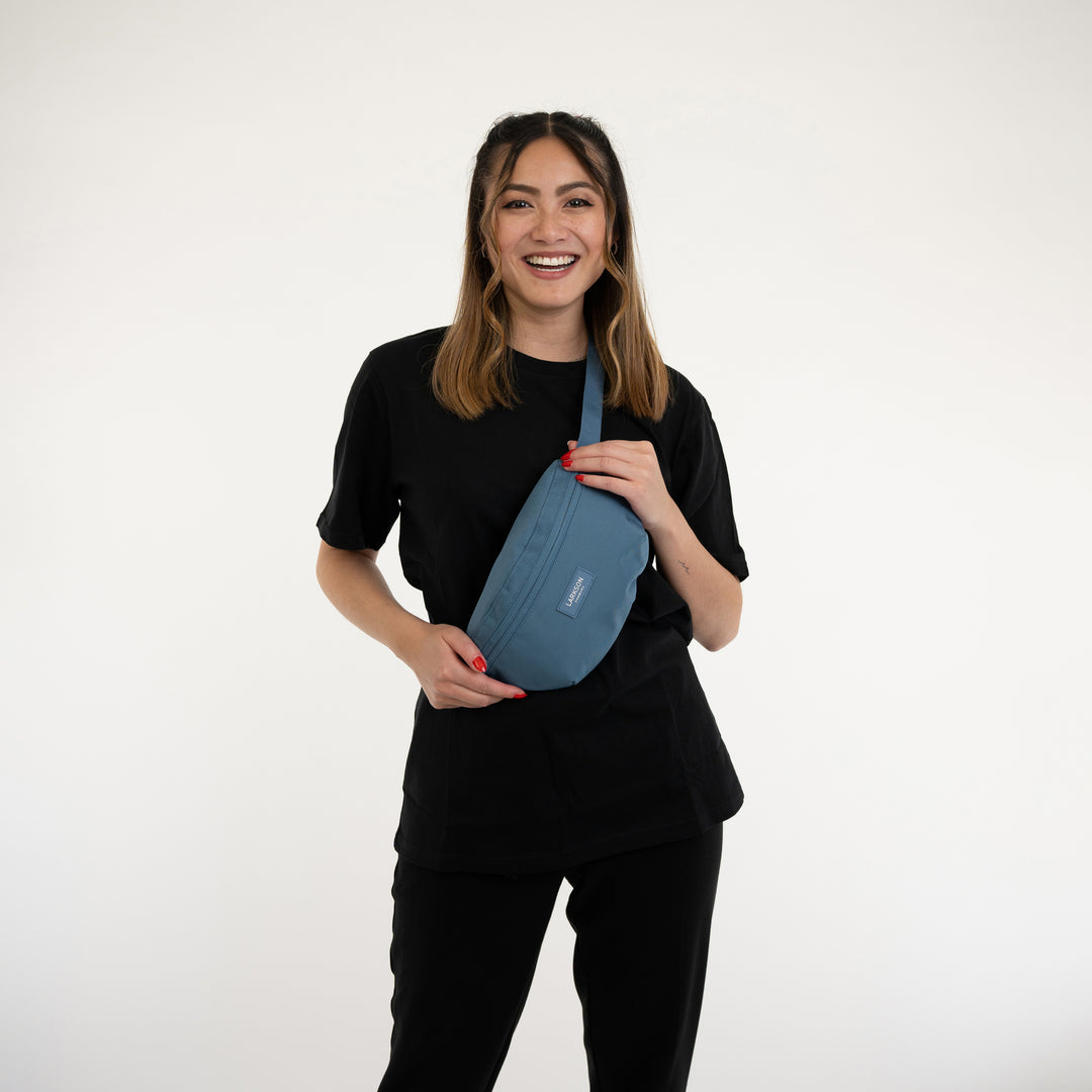 Frau trägt blaue Larkson Bauchtasche Finn über der Schulter, schwarzes Outfit