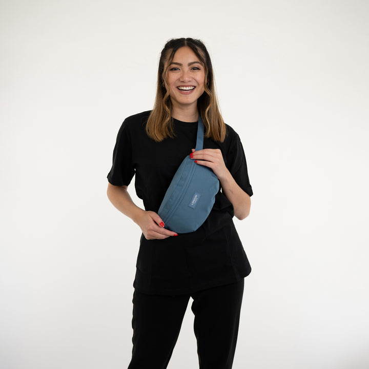 Frau trägt blaue Larkson Bauchtasche Finn über der Schulter, schwarzes Outfit