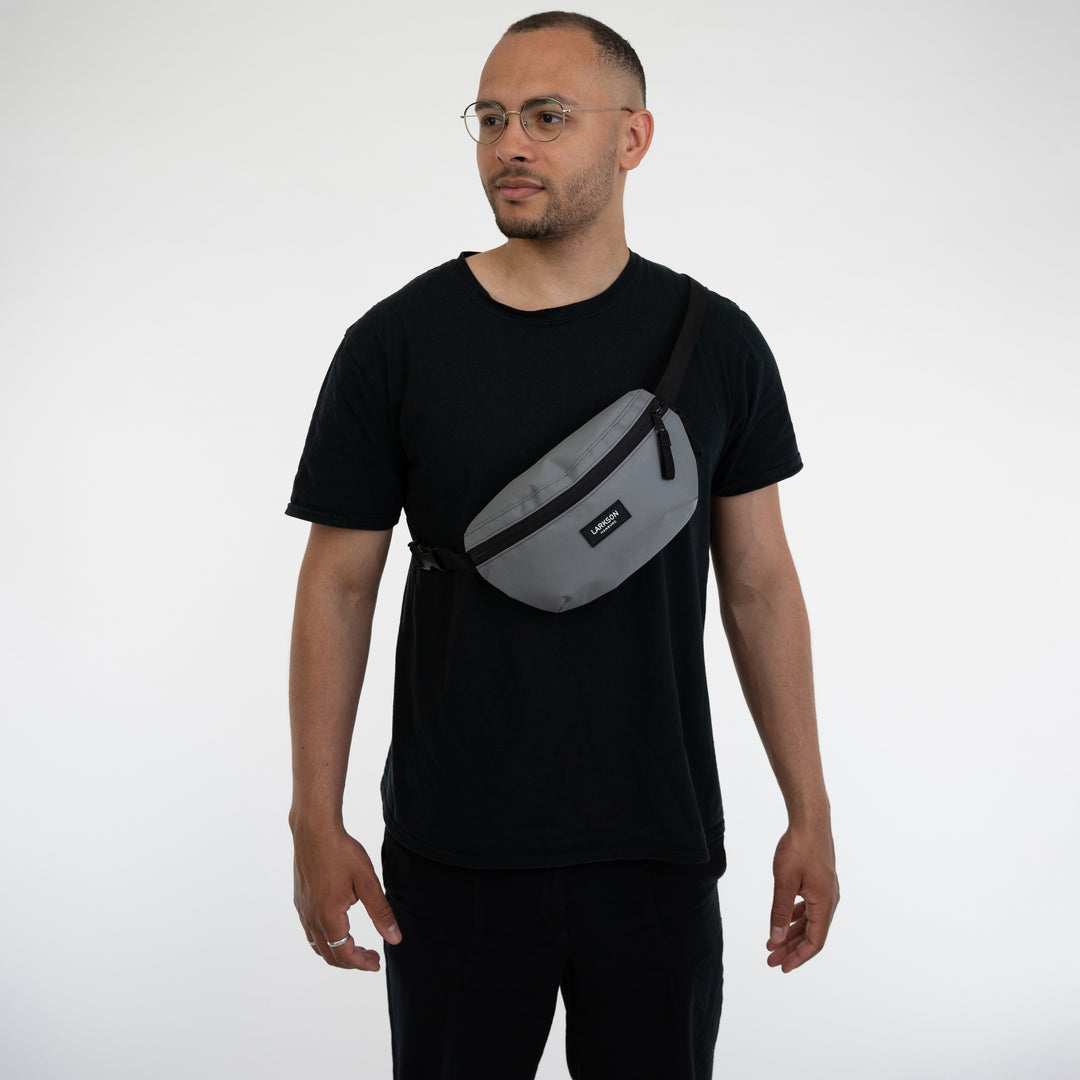 Mann trägt graue Bauchtasche 'Finn' von LARKSON quer über die Brust, schwarzes T-Shirt und Brille