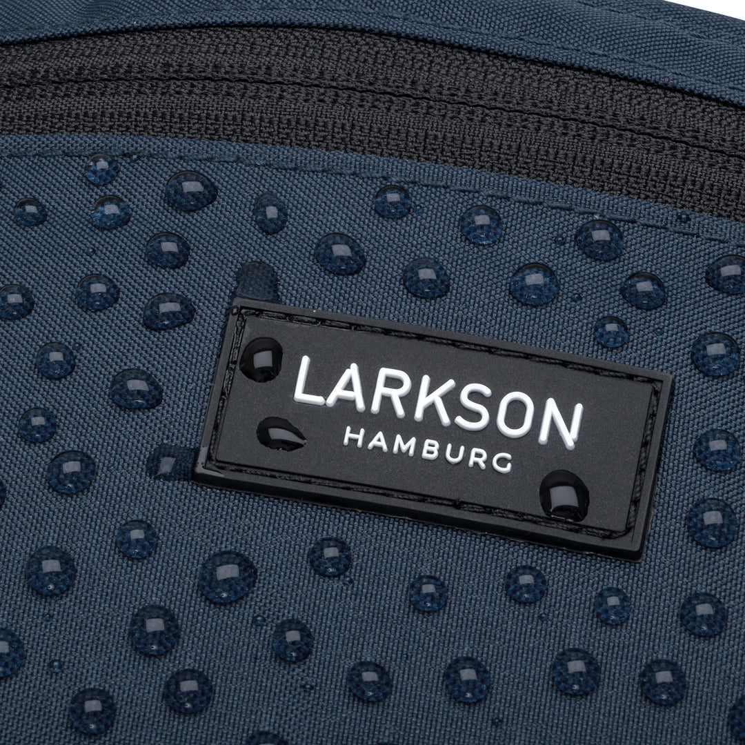 Nahaufnahme der wasserabweisenden blauen Bauchtasche Finn von Larkson mit Regentropfen auf dem Stoff und Label