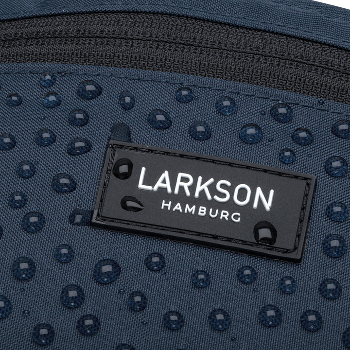 Nahaufnahme der wasserabweisenden blauen Bauchtasche Finn von Larkson mit Regentropfen auf dem Stoff und Label