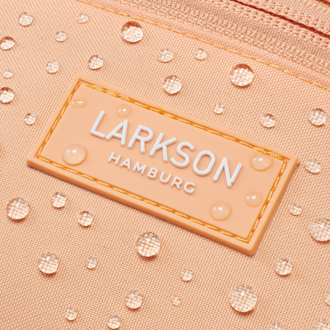 Nahaufnahme eines wasserabweisenden peachfarbenen Stoffes mit LARKSON Hamburg Logo und Wassertropfen