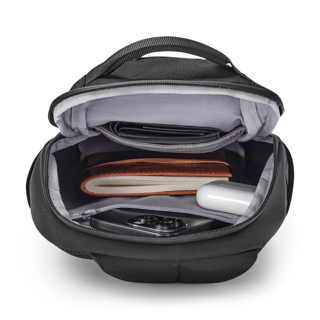 Schwarze Sling Bag Klint mit offenem Hauptfach, darin ein Notizbuch, ein Smartphone, Ohrhörer und eine Brieftasche