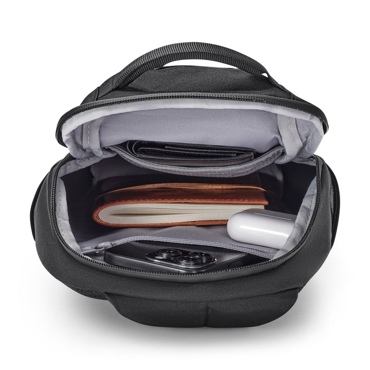 Schwarze Sling Bag Klint mit offenem Hauptfach, darin ein Notizbuch, ein Smartphone, Ohrhörer und eine Brieftasche