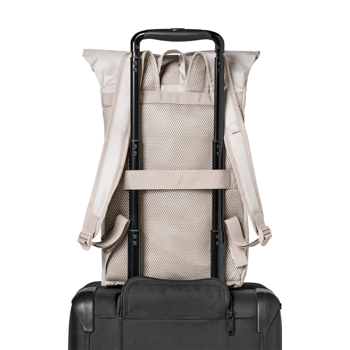 Beiger faltbarer Rolltop Rucksack Arne, befestigt am Griff eines schwarzen Reisekoffers