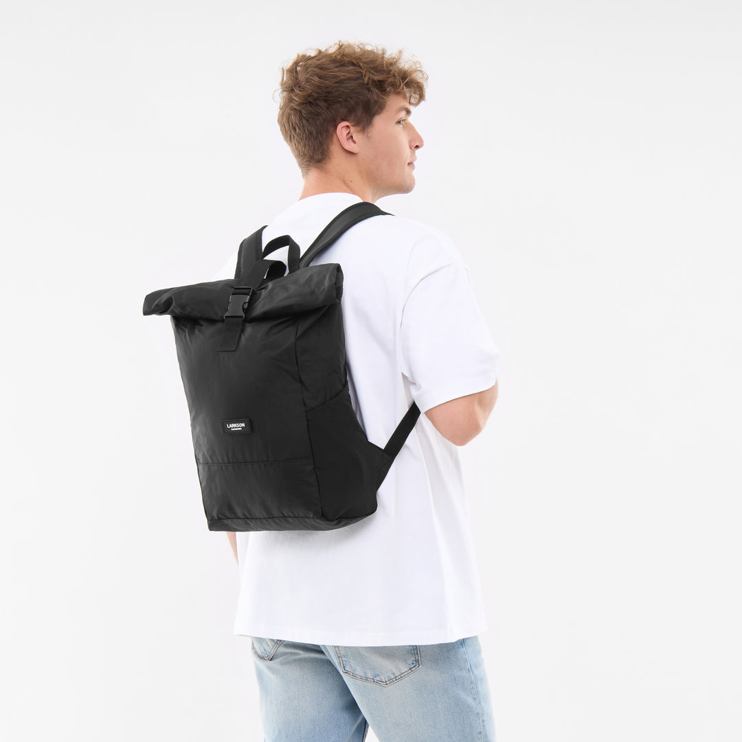 Mann mit weißem T-Shirt und hellem Jeansstoff trägt faltbaren schwarzen Rolltop Rucksack Arne von LARKSON
