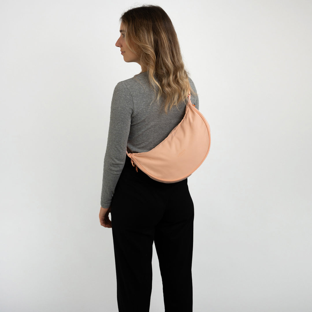 Frau von hinten mit grauem Pullover, schwarzer Hose und peachfarbener 'Half Moon Bag Solveig Medium' von LARKSON