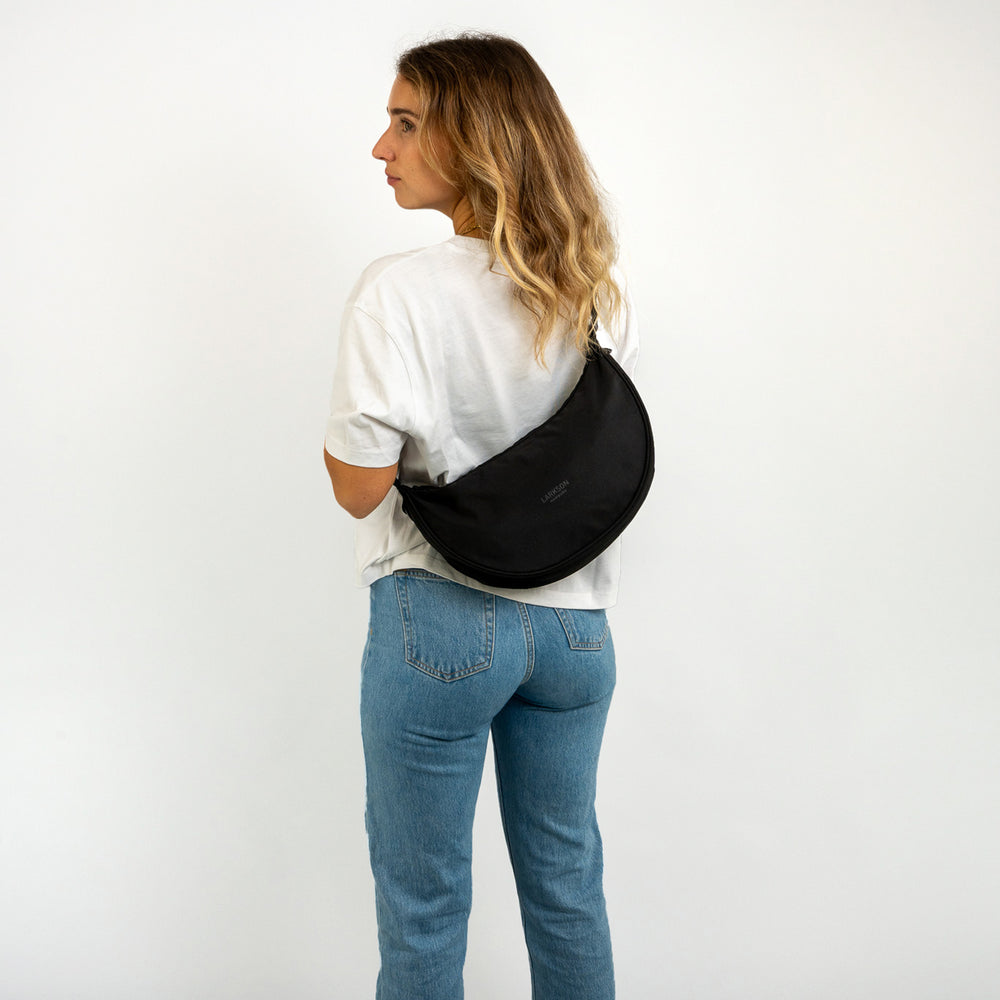 Frau mit halbrunder schwarzen Half Moon Bag Solveig Medium von LARKSON über der Schulter, weißes T-Shirt, blaue Jeans