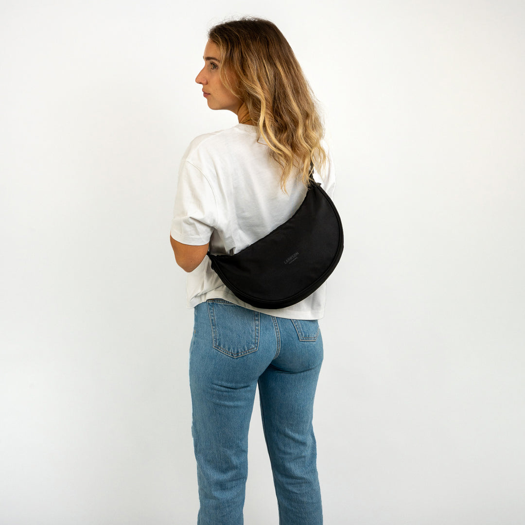 Frau mit halbrunder schwarzen Half Moon Bag Solveig Medium von LARKSON über der Schulter, weißes T-Shirt, blaue Jeans