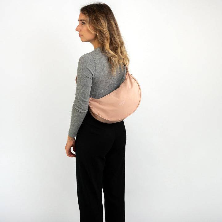 Frau mit langen blonden Haaren trägt halbrunden rosa Half Moon Bag Solveig Medium von LARKSON über der Schulter