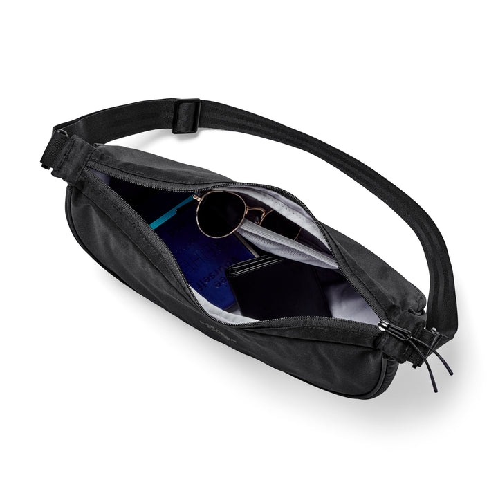 Schwarze Half Moon Bag Solveig Medium mit geöffnetem Reißverschluss, gezeigt werden Innenfächer mit Sonnenbrille, Geldbörse und Notizbuch