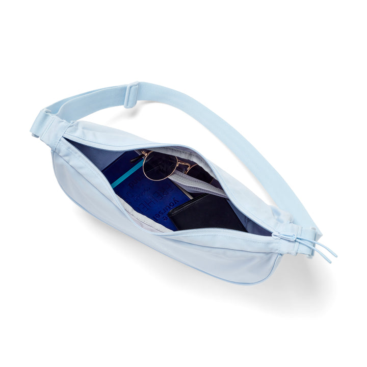 Halbmondtasche Solveig Medium in eisblau mit verstellbarem Riemen, geöffnet mit blaue Buch, Sonnenbrille und schwarzer Geldbörse innen