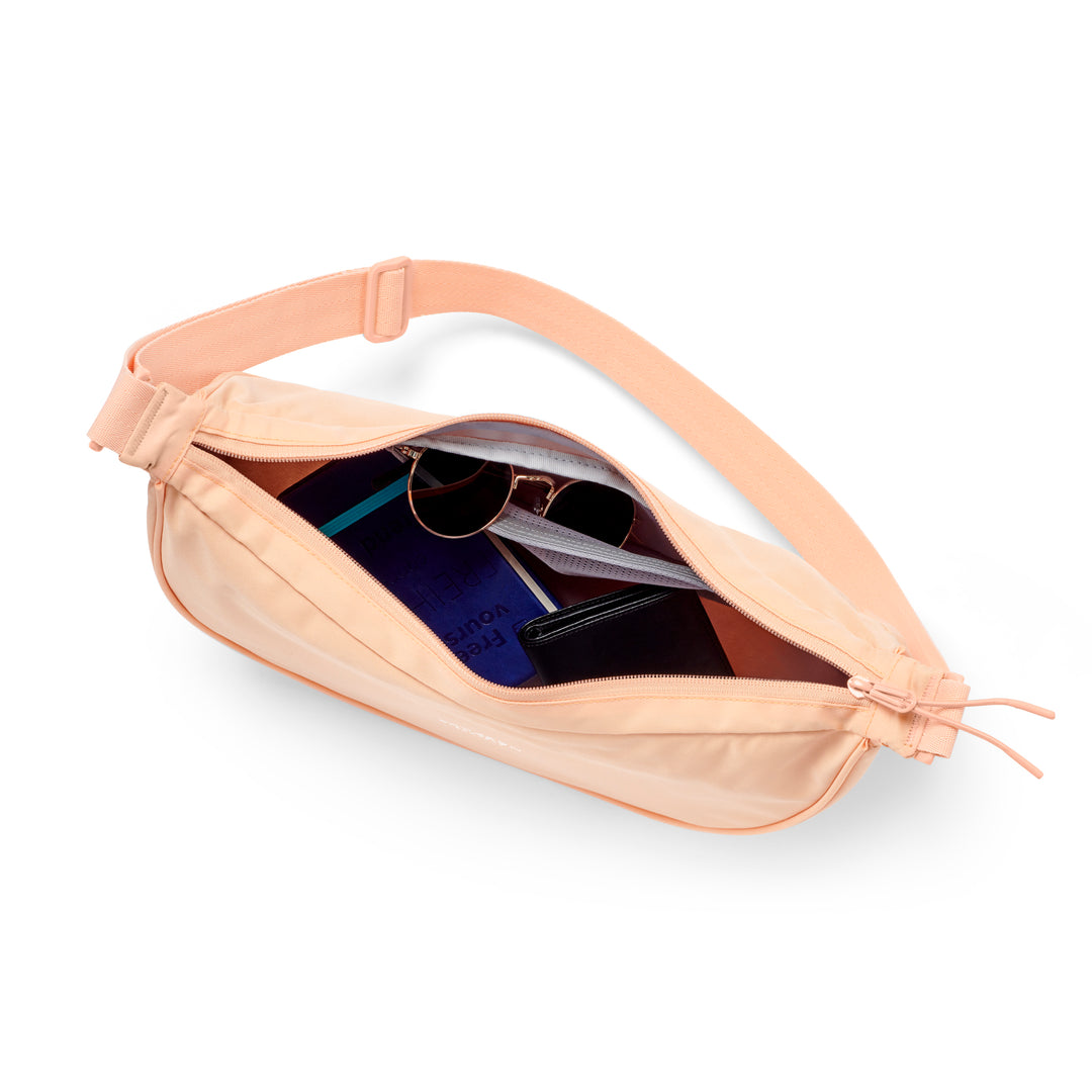 Halbmond-Tasche Solveig Medium in Pfirsich mit verstellbarem Schulterriemen, geöffnet mit sichtbarem Inhalt wie Sonnenbrille und Portemonnaie