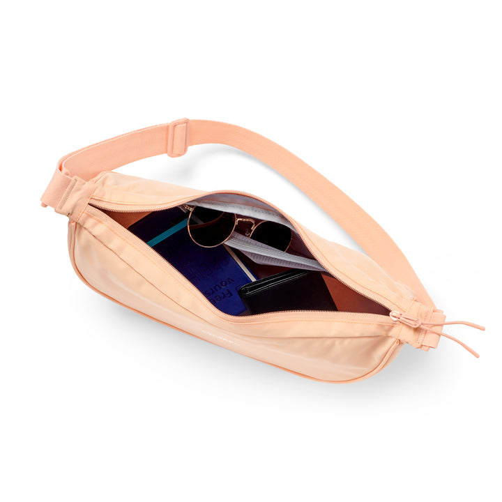 Halbmond-Tasche Solveig Medium in Pfirsich mit verstellbarem Schulterriemen, geöffnet mit sichtbarem Inhalt wie Sonnenbrille und Portemonnaie