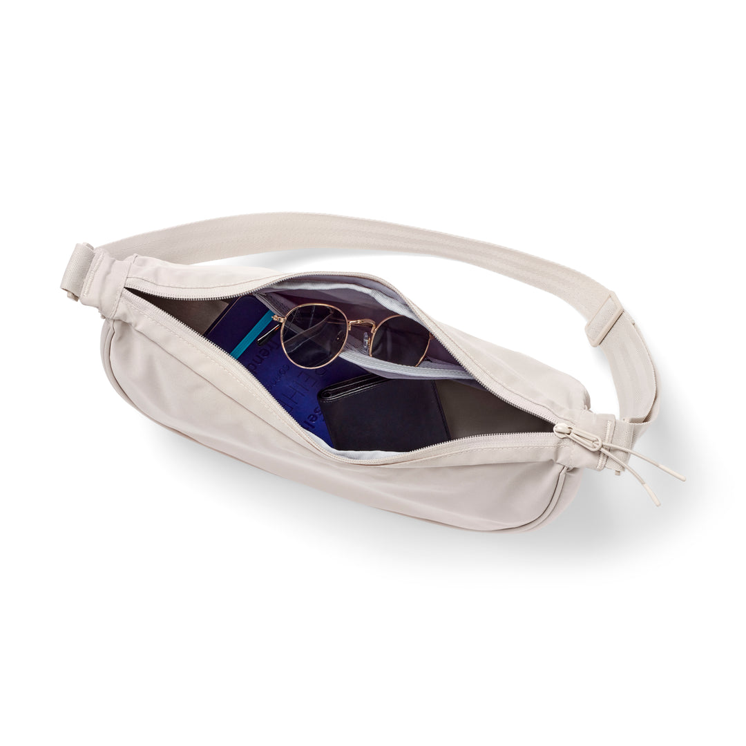 Halbmond-Tasche Solveig Medium in Sandfarbe mit verstellbarem Träger, geöffnet und befüllt mit Sonnenbrille, Notizbuch und Geldbörse
