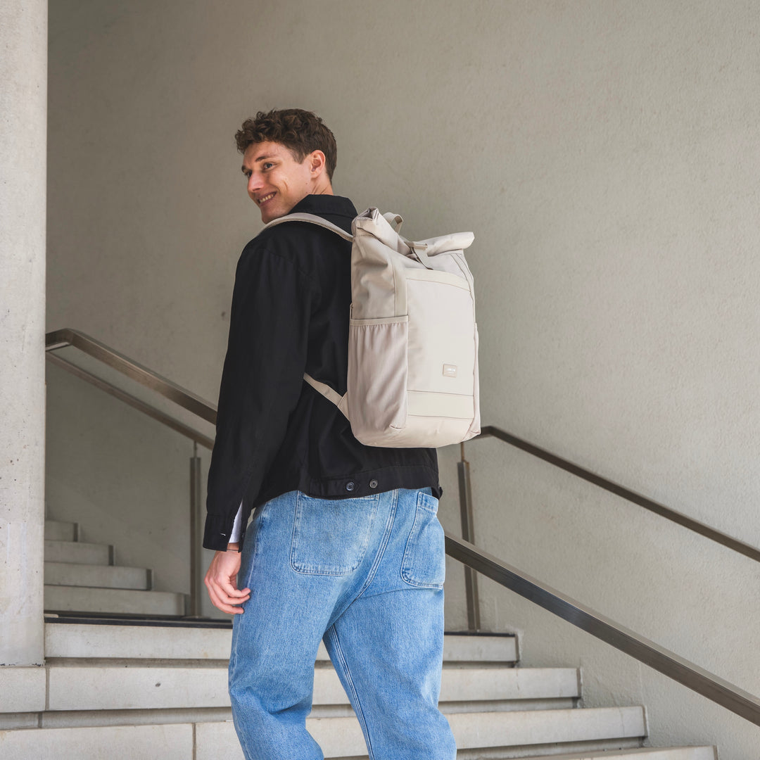 Beiger Rolltop Rucksack No 2 von Larkson an einem Mann mit schwarzer Jacke und blauen Jeans auf einer Treppe