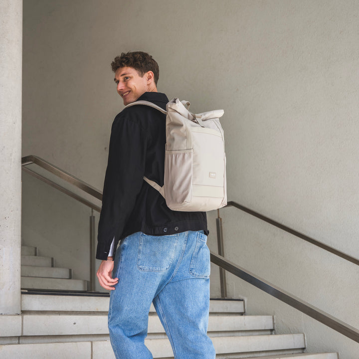 Beiger Rolltop Rucksack No 2 von Larkson an einem Mann mit schwarzer Jacke und blauen Jeans auf einer Treppe