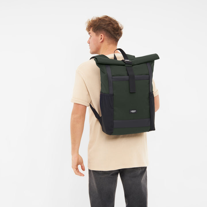 Mann trägt olivgrünen Larkson Rolltop Rucksack No 2 mit schwarzem Verschluss und Seitentaschen