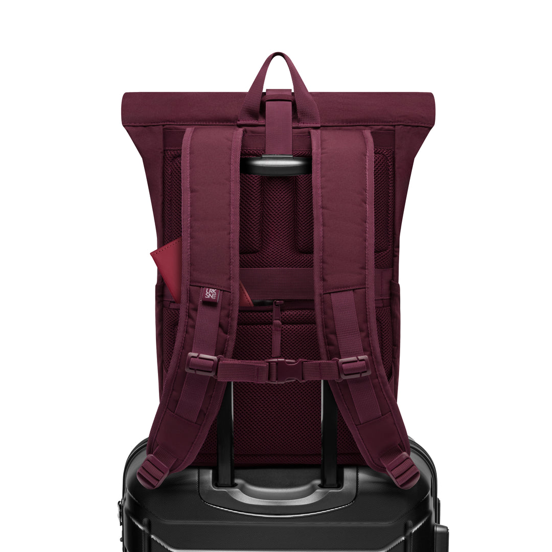 Rolltop Rucksack No 4 in Beerentönen auf einem schwarzen Hartschalenkoffer mit ausgezogenem Griff
