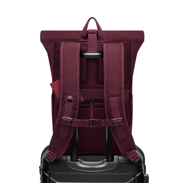 Rolltop Rucksack No 4 in Beerentönen auf einem schwarzen Hartschalenkoffer mit ausgezogenem Griff