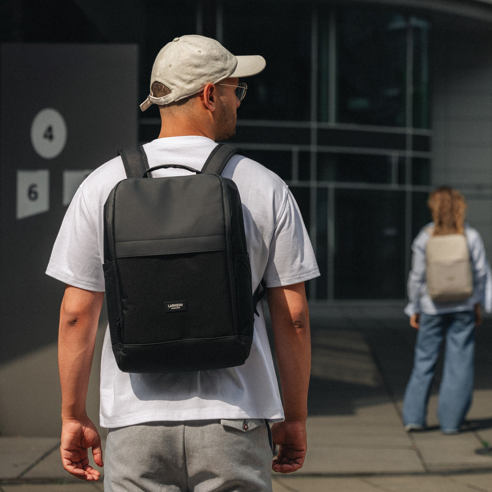 Mann mit hellem Cap und weißem T-Shirt trägt schwarzen LARKSON Rucksack Niklas in urbaner Umgebung