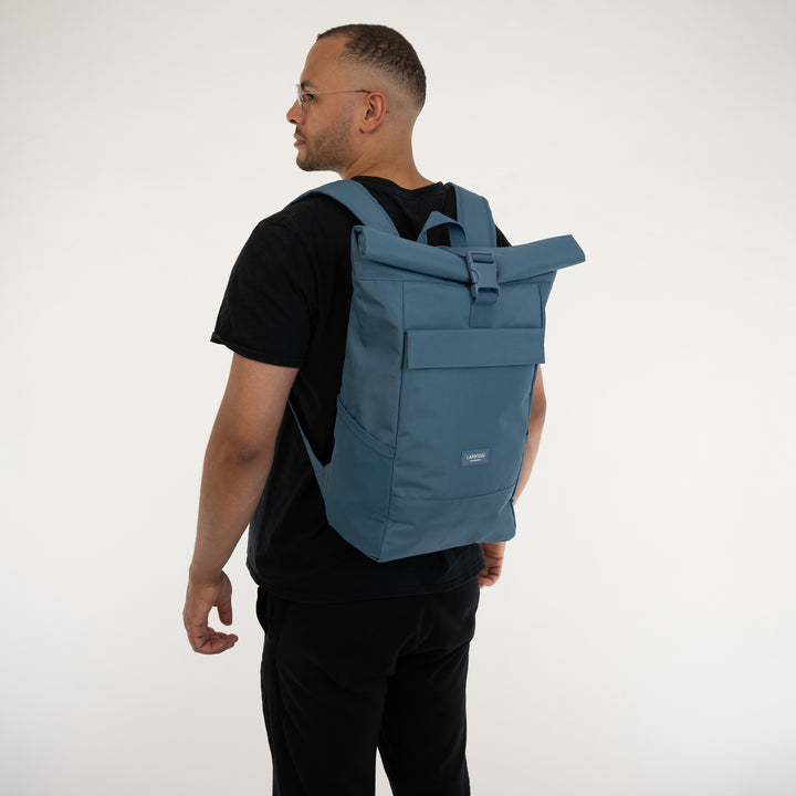 Mann trägt blauen LARKSON Rolltop Rucksack No 4 mit schwarzem T-Shirt und Hose