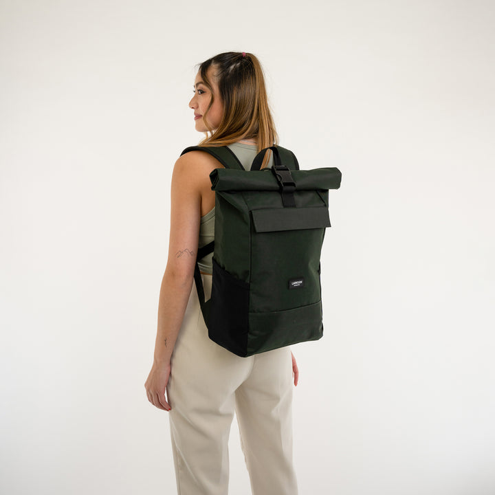 Frau trägt dunkelgrünen Rolltop Rucksack No 4 von LARKSON, graues Tanktop, helle Hose