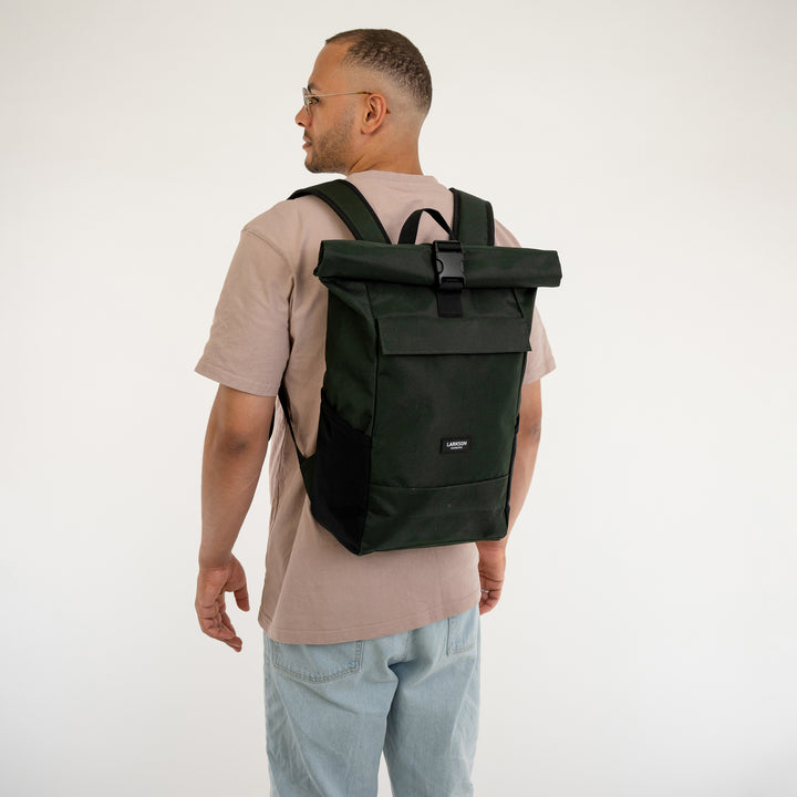 Mann trägt dunkelgrünen Rolltop Rucksack No 4 von LARKSON mit Schnallenverschluss und gepolsterten Schultergurten