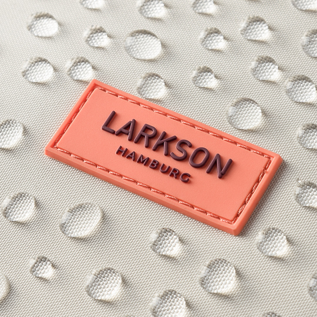 Nahaufnahme des wasserabweisenden Materials eines sandrosafarbenen Rolltop Rucksacks No 4 mit aufgenähtem LARKSON Hamburg Emblem