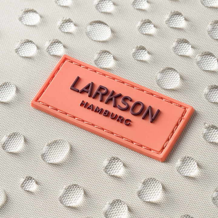 Nahaufnahme des wasserabweisenden Materials eines sandrosafarbenen Rolltop Rucksacks No 4 mit aufgenähtem LARKSON Hamburg Emblem