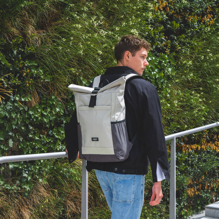 Mann trägt beigen und grauen Rolltop Rucksack No 2 von Larkson mit schwarz-grauer Jeansjacke und blauen Jeans