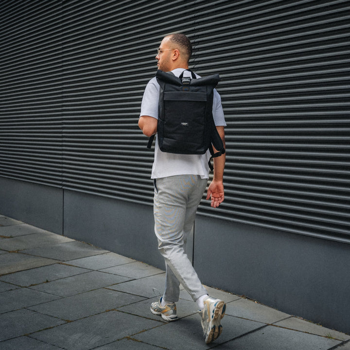 Mann läuft an einer schwarzen Wand entlang mit einem schwarzen Rolltop Rucksack No 4 von LARKSON