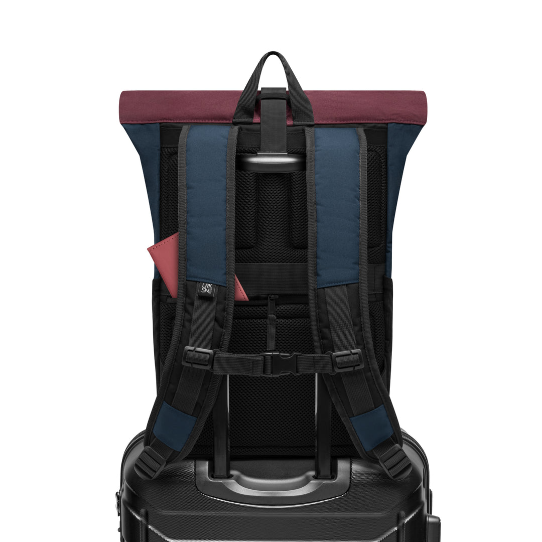 Rückansicht des Rolltop Rucksacks No 4 in blau mit beerfarbenem Rolltop, befestigt auf einem schwarzen Trolleygriff