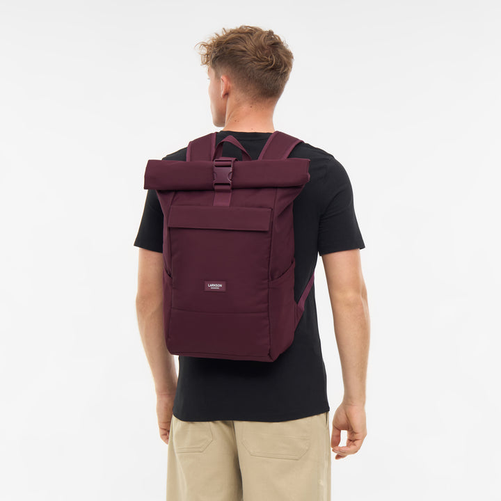 Herren mit schwarzem T-Shirt trägt LARKSON Rolltop Rucksack No 4 in Beerenton von hinten