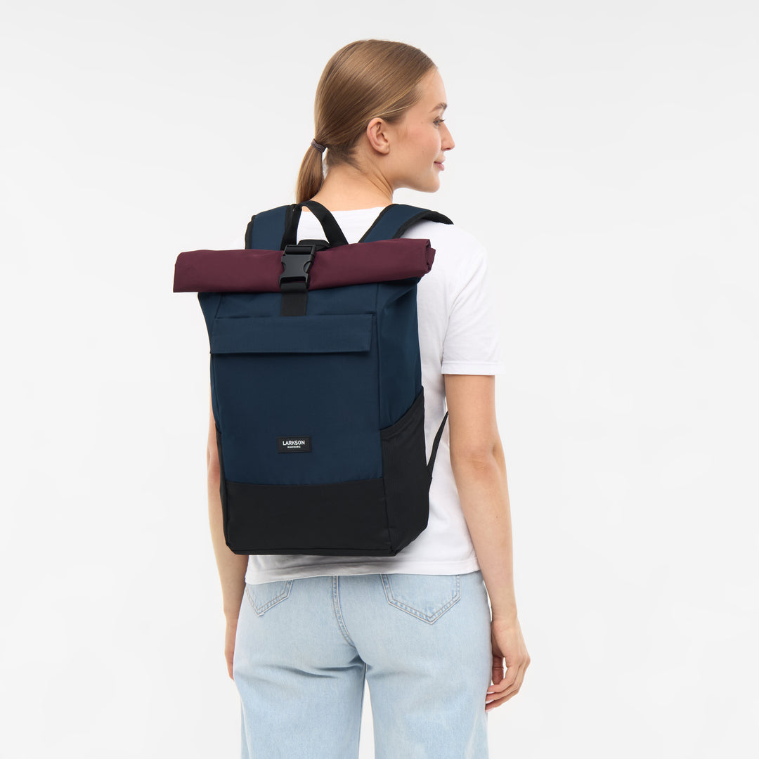 Frau mit Rolltop Rucksack No 4 von LARKSON in Blau, Schwarz und Berry, trägt weißen T-Shirt und blaue Jeans