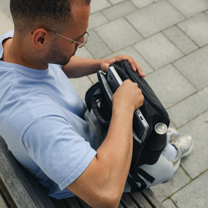 Mann legt Laptop in schwarzen Rucksack Niklas mit Seitentasche für Getränk