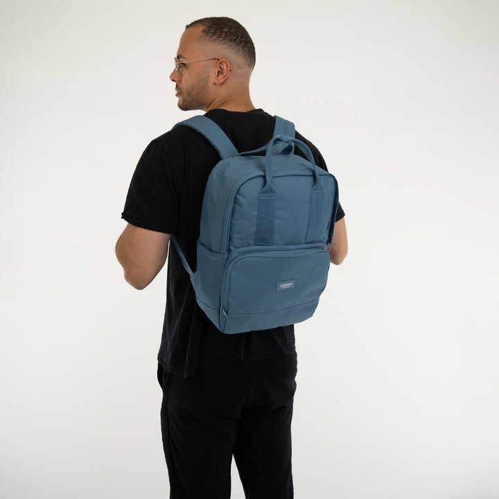 Mann trägt blauen LARKSON Rucksack No 6 mit zwei Tragegriffen und Fronttasche